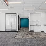 The image shows a modern office space with white cabinets, dark countertops, a glass door, a teal accent wall, and gray carpeting.